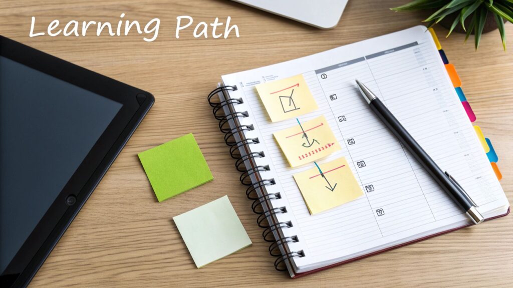Overhead view of a workspace with a tablet, a spiral notebook, and sticky notes outlining a learning path.